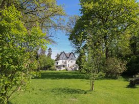 A large house with surrounding trees and a green lawn at Serenity House The Retreat in Llangammarch Wells near Llanwrtyd Wells