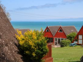 A seaside view with red A-frame houses green grass and bushes at Chalet 58 - The Beach House in Kingsdown