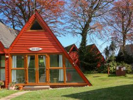 A red wooden triangular house with glass doors and windows surrounded by trees and grass at Chalet 58 - The Beach House in Kingsdown