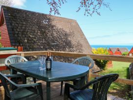 A balcony with a plastic table and chairs with a bottle and glasses overlooking rooftops and the sea at Chalet 58 - The Beach House in Kingsdown