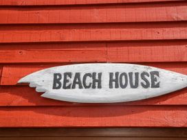 A wooden sign reading BEACH HOUSE mounted on a red wooden wall at Chalet 58 - The Beach House in Kingsdown