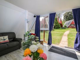 A living room with a black sofa and flowers on a table next to a glass door with blue curtains showing a garden outside at Chalet 58 - The Beach House in Kingsdown