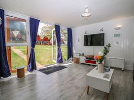 A living room with a coffee table with flowers a wall mounted TV and large glass doors with blue curtains at Chalet 58 - The Beach House in Kingsdown