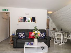 A living room with a black leather sofa and nautical themed pillows a white coffee table with flowers and magazines and a small dining table with chairs at Chalet 58 - The Beach House in Kingsdown