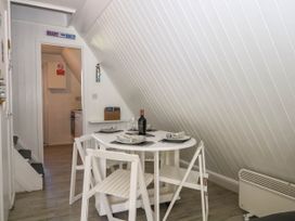 A dining area with a round table set for four with white chairs under a slanted ceiling at Chalet 58 - The Beach House Kingsdown