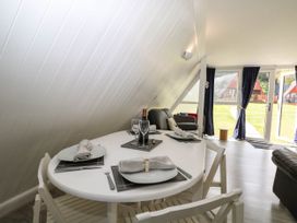 A dining table set for four with plates and napkins next to a living area with chairs and large windows at Chalet 58 - The Beach House in Kingsdown
