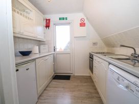 A compact kitchen with white cabinets a fridge dishwasher sink stove and a door with fire exit sign at Chalet 58 - The Beach House in Kingsdown