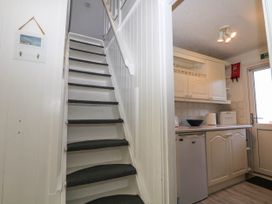A staircase with dark carpeted steps next to a kitchen area with white cabinets and appliances at Chalet 58 - The Beach House in Kingsdown