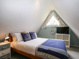 A bedroom with a double bed, bedside table, television on a stand, and a triangular window with curtains at Chalet 58 - The Beach House in Kingsdown