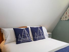 A bed with white sheets and two navy blue pillows with sailboat designs next to a small white bedside table at Chalet 58 - The Beach House in Kingsdown