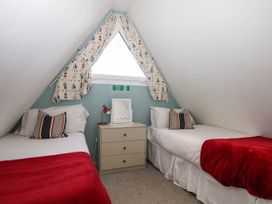 A bedroom with two single beds a nightstand with a lamp and a window with patterned curtains at Chalet 58 - The Beach House in Kingsdown