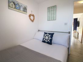 A small bedroom with a bed with white sheets and pillows and a navy pillow with a ship wheel design at Chalet 58 - The Beach House in Kingsdown