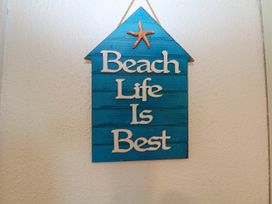 A blue wooden wall hanging shaped like a house with a starfish and the words Beach Life Is Best on a textured white wall at Chalet 58 - The Beach House in Kingsdown