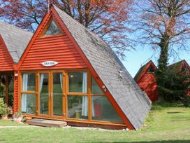 A red wooden triangular cabin with glass doors and windows on grassy land at Chalet 58 - The Beach House in Kingsdown