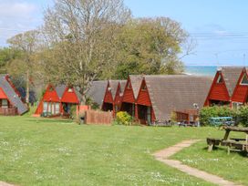 A row of red triangular wooden cabins with a grassy area and trees at Chalet 58 - The Beach House in Kingsdown