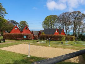 A sandy volleyball court with a net in front of red triangular cabins and a mini golf course at Chalet 58 - The Beach House in Kingsdown