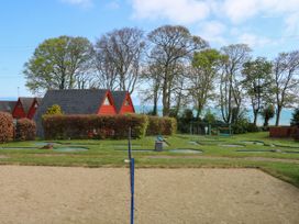 A sandy volleyball court with a net in front of red triangular cabins and trees by the sea at Chalet 58 - The Beach House in Kingsdown