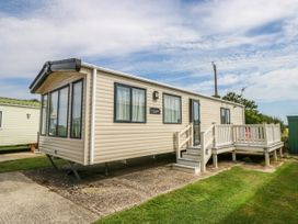 A beige mobile home with multiple windows and a small porch with steps on a lawn at Coastal Cottage in East Wittering
