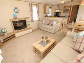 A living room with beige sofas and a wooden coffee table next to a dining area and kitchen at Coastal Cottage in East Wittering