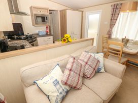 A kitchen with stove microwave and pantry and a beige sofa with patterned cushions and a dining table with chairs in a room at Coastal Cottage in East Wittering