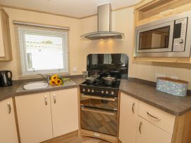 A kitchen corner with a sink a bouquet of sunflowers a kettle a stove with pots a microwave and a tin container at Coastal Cottage in East Wittering