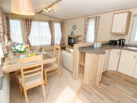An open plan dining area with a wooden table and four chairs next to a kitchen with cream cabinets and a living room with a sofa and a TV at Coastal Cottage in East Wittering