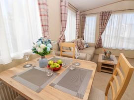 A dining table with glasses and a bowl of apples next to a sofa with cushions and a coffee table with a wine cooler at Coastal Cottage in East Wittering