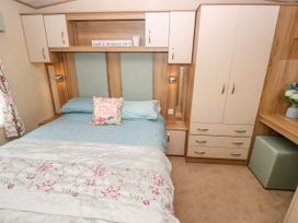 A bedroom with a bed blue bedding a floral pillow built in cabinets a wardrobe and a small green ottoman at Coastal Cottage in East Wittering