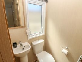 A small bathroom with a toilet and pedestal sink under a frosted window at Coastal Cottage in East Wittering