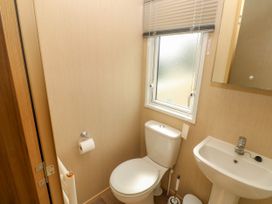 A small bathroom with a toilet next to a window and a pedestal sink at Coastal Cottage in East Wittering