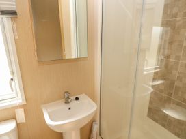 A bathroom with a pedestal sink a mirror a window a toilet and a glass shower enclosure at Coastal Cottage in East Wittering