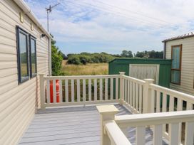 An outdoor deck area with railing between two mobile homes and a green shed in the background at Coastal Cottage in East Wittering