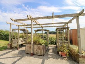 An outdoor wooden pergola structure with built-in benches and planter boxes with shrubs at Coastal Cottage in East Wittering