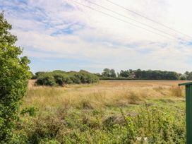 An open field with tall grass and bushes under a partly cloudy sky at Coastal Cottage in East Wittering