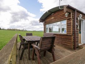 An outdoor wooden deck with a table and four chairs next to a wooden cabin in a grassy field at Hollie in Raglan