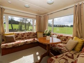 A seating area with a patterned corner sofa cushions and a round wooden table with flowers in a room with large windows at Hollie in Raglan