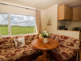 A dining area with a round wooden table and patterned corner seating next to a large window showing a green field at Hollie in Raglan