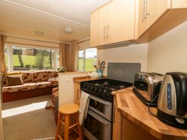 A kitchen area with stove toaster and kettle next to a seating area with couch and table at Hollie in Raglan