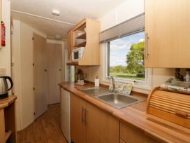 A kitchen with a sink under a window an electric kettle a microwave and wooden cabinets at Hollie in Raglan