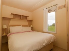 A bedroom with a double bed two bedside lamps a window with a curtain and a shelf above the bed at Hollie in Raglan