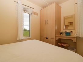 A bedroom with a bed a window with curtains a wooden wardrobe and a dressing table with a stool at Hollie Raglan