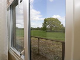 A view through a window showing a wooden railing outside with a green field and tree in the background at Hollie in Raglan