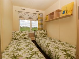 A bedroom with two single beds with leaf patterned bedding a window with animal print blinds and a shelf with yellow cushions at Hollie in Raglan