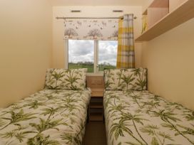 A bedroom with two single beds with leaf patterned bedding and a window with animal print blind at Hollie in Raglan