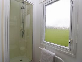 A shower with glass door next to a frosted window and a towel on a rack at Hollie in Raglan