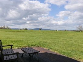 A wooden bench and table on a deck overlooking a grassy field with distant hills and clouds at Hollie in Raglan