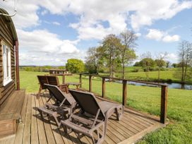 A wooden deck with lounge chairs and a table overlooking a grassy field and a river at Poppy in Raglan