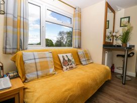 A living room with a yellow sofa and plaid cushions near a window and a corner desk with a mirror and lamp at Poppy in Raglan