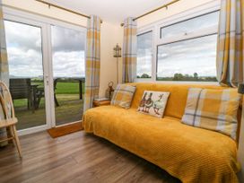 A living room with a yellow covered sofa and plaid curtains by glass doors overlooking a deck and green field at Poppy in Raglan