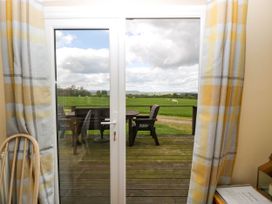 A patio door opening to a wooden deck with outdoor chairs and table overlooking a green field with sheep at Poppy in Raglan